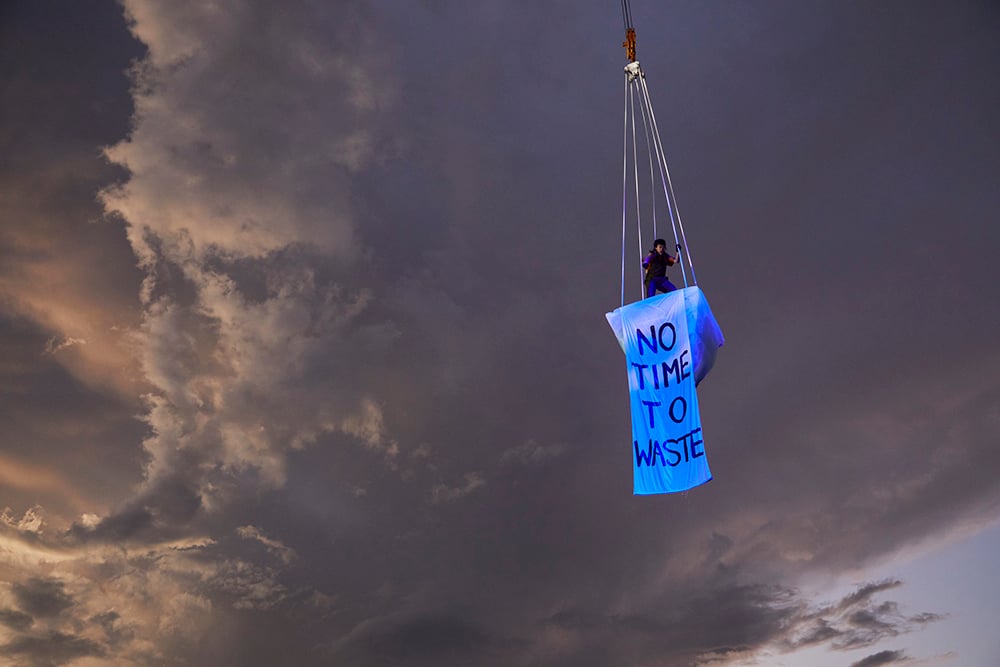 Image: Isabel Estrella performing in THAW - Shane Rozario. An Ice Structure suspended - storm clouds in the background. A suspended banner reads: 