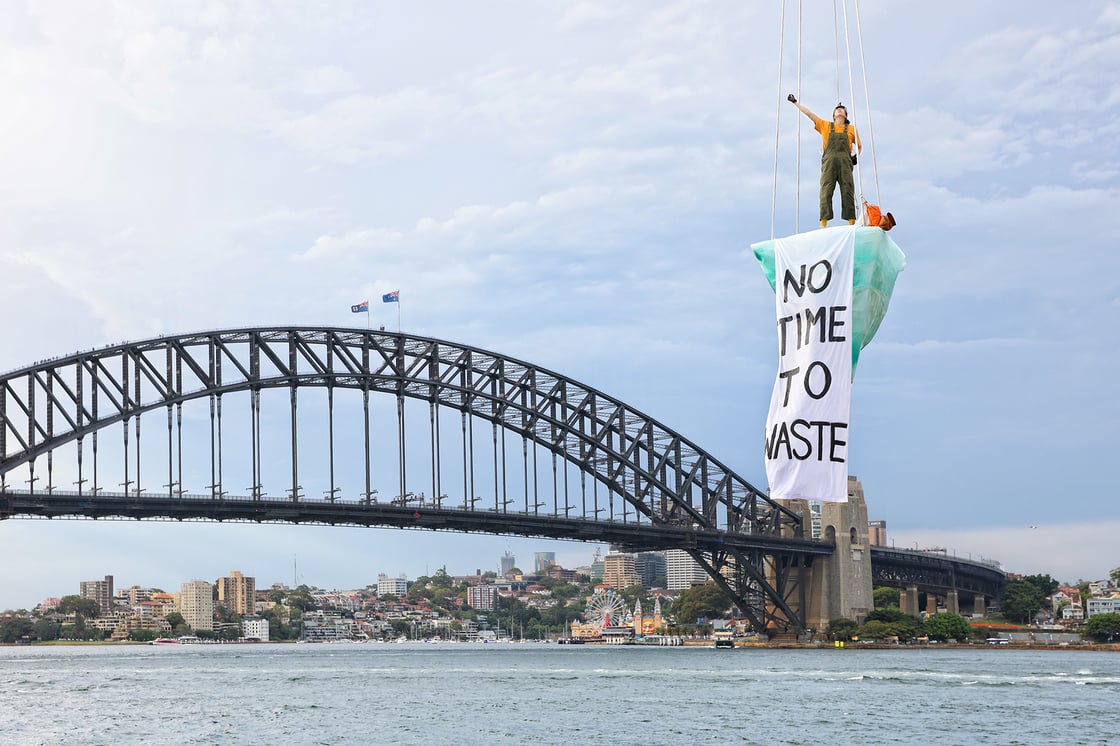 Isabel Estrella suspended on the Ice Sculpture for THAW over Sydney Harbour, a banner unfurled reads 